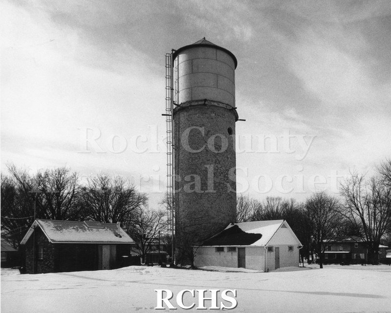 Black and white photograph of the Clinton Water Tower with a small building beside it and another building on the left.