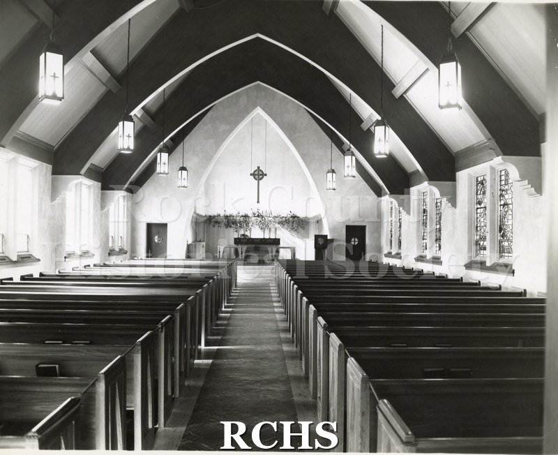 Black and white photograph of the interior of Immanuel Lutheran, Wausau, WI, showing pews leading up to the altar with a cross suspended above it.