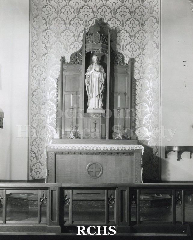 Black and white photograph of the interior of an unidentified church showing the altar with a statue of Christ in a niche behind it.