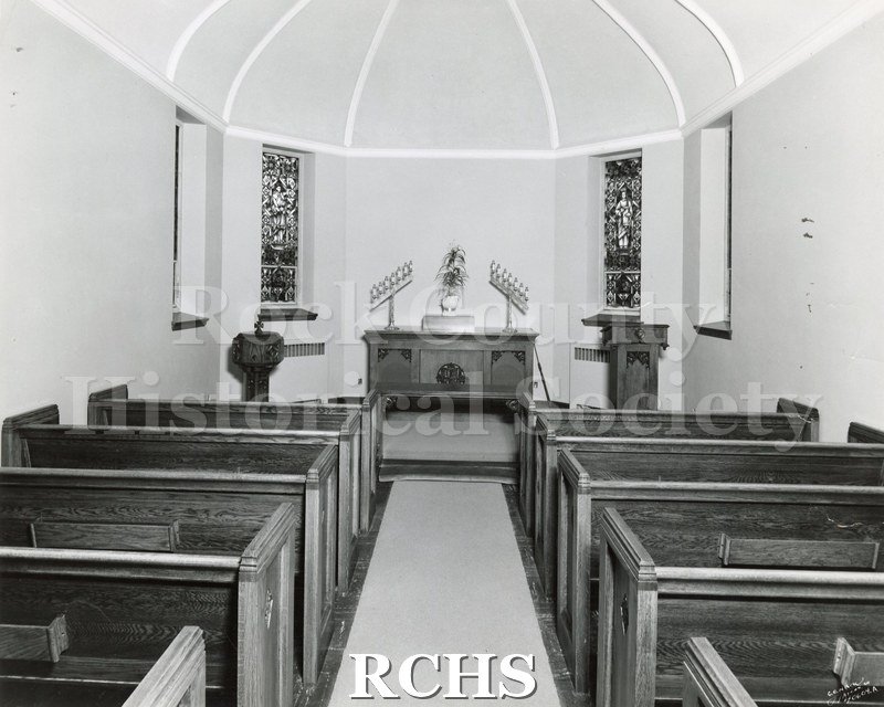 Black and white photograph of the interior of an unidentified church, showing pews leading up to the altar.