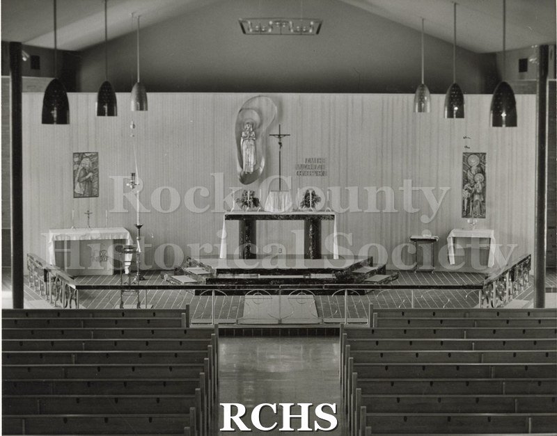 Black and white photograph of the interior of Our Lady of Lourdes Roman Catholic Church, Genoa, OH, with a long communion railing in front of a plain altar.