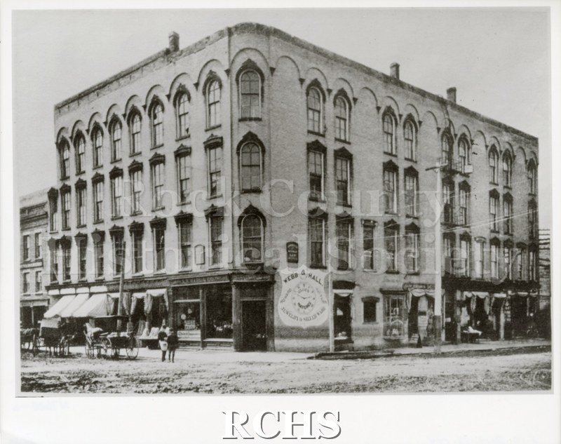 Black and white photograph of a four story building with a sign: "Webb & Hall" "Jewelry and Silverware" on the side.