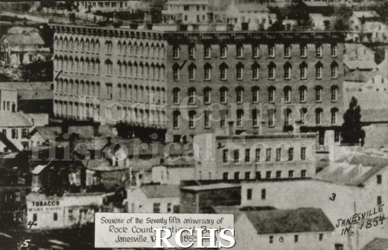 Black and white photograph of early Janesville. On front: "Souvenir of the Seventy fifth anniversary of Rock County National Bank Janesville, Wis.