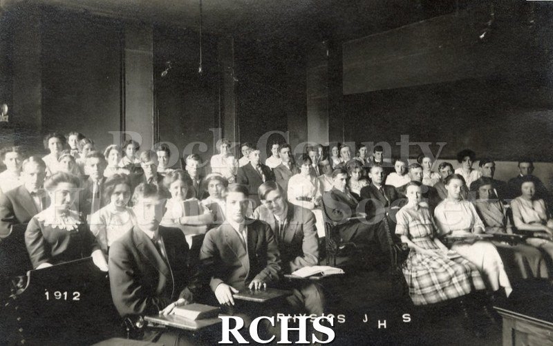 Postcard. Black and white photograph of the 1912 Physics class at Janesville High School. Students are seated at their desks.