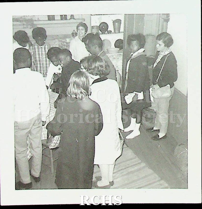 Black and white photograph of Mrs. Charles Norris and Franklin Junior High 8th Grade. Shows several students listening to the docent at the Tallman House.
