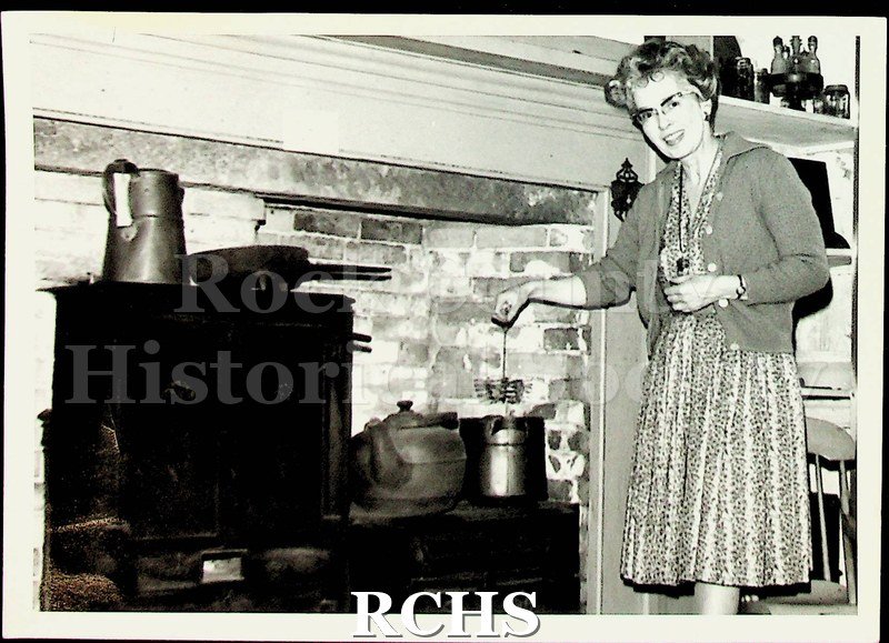 Black and white photograph of Ruth Hughes. She is the docent demonstrating cooking on the stove in the basement of the Tallman House.