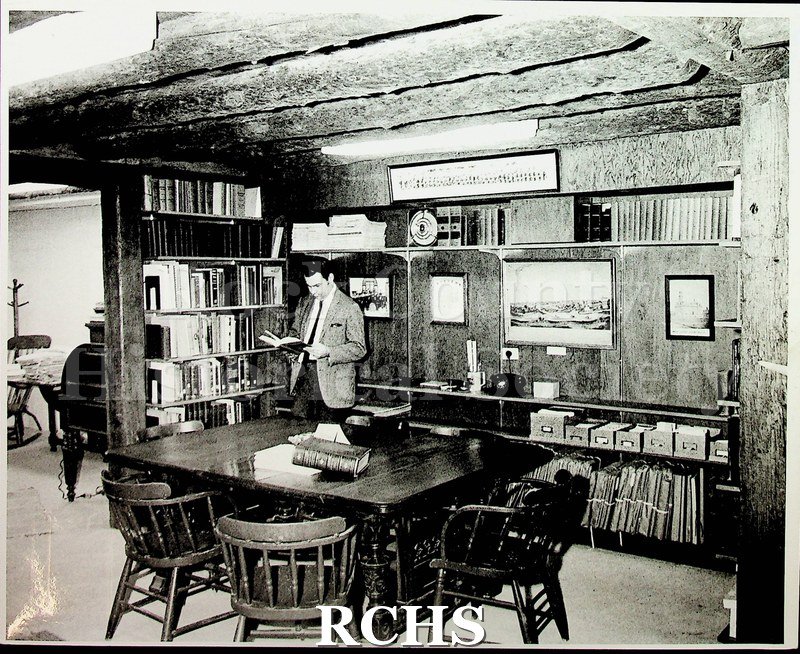 Black and white photograph of Richard Hartung. He's reading a book in a library.