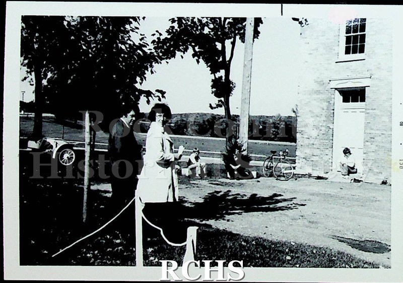 Black and white photograph of several unidentified people near the carriage house. An antique car is visible on the left.