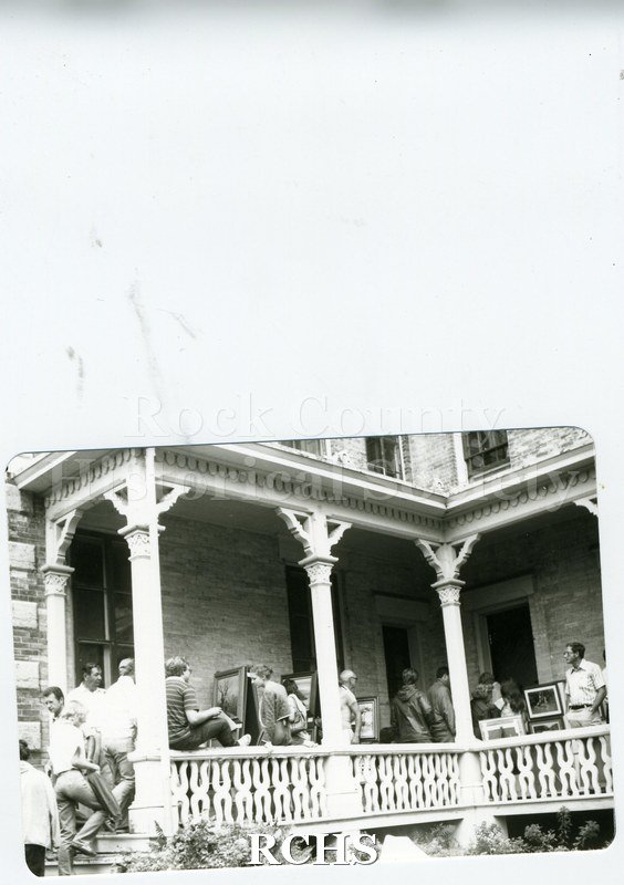 Black and white photograph of several unidentified people on the porch of the Tallman House where paintings are displayed.