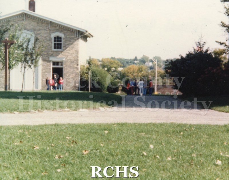 Color photo of a school tour, showing a few students in front of the Tallman Carriage House.