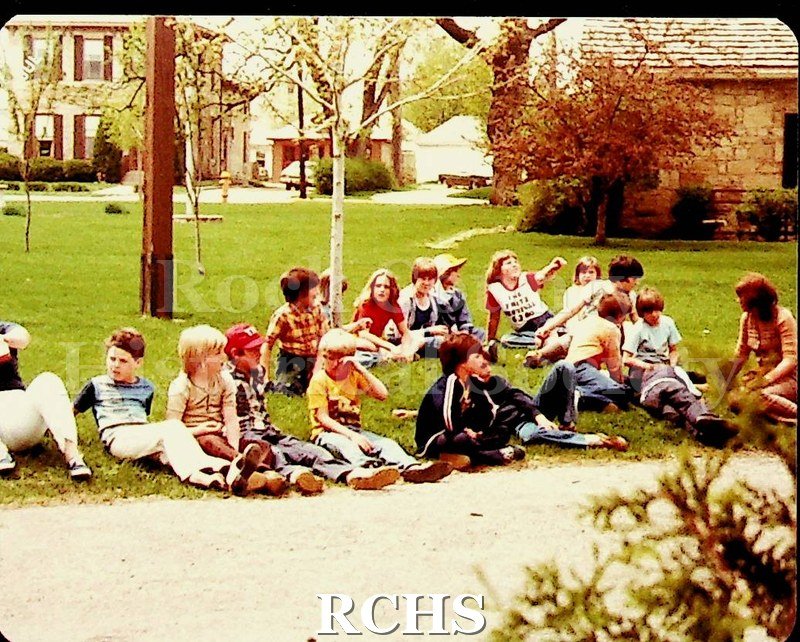 Color photo of students from East View, Lake Geneva, sitting on the lawn at the Tallman House.