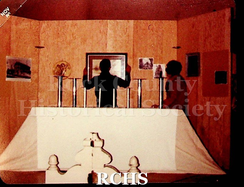 Color photo of Maurice Montgomery hanging a picture while a woman looks on.