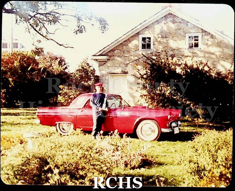 Color photo of David Quass standing near an antique red car in front of the Stone House.