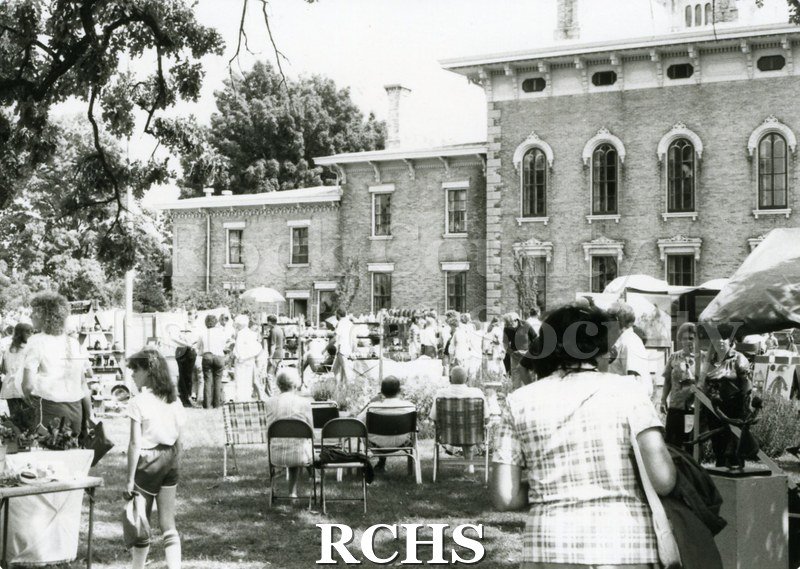 Black and white photograph of the 1981 Tallman Art Festival. People are strolling the lawn by the Tallman House. Several people are sitting in lawn chairs.