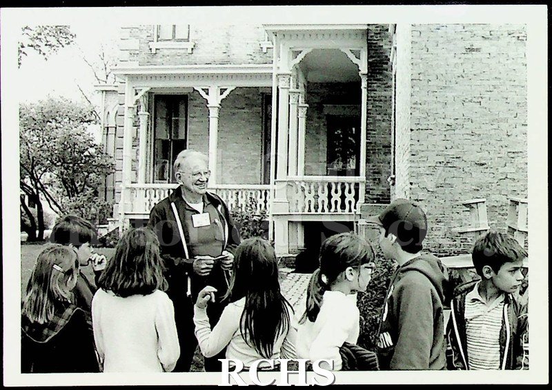 Black and white photograph of unidentified school group standing in front of the Tallman House with the docent.
