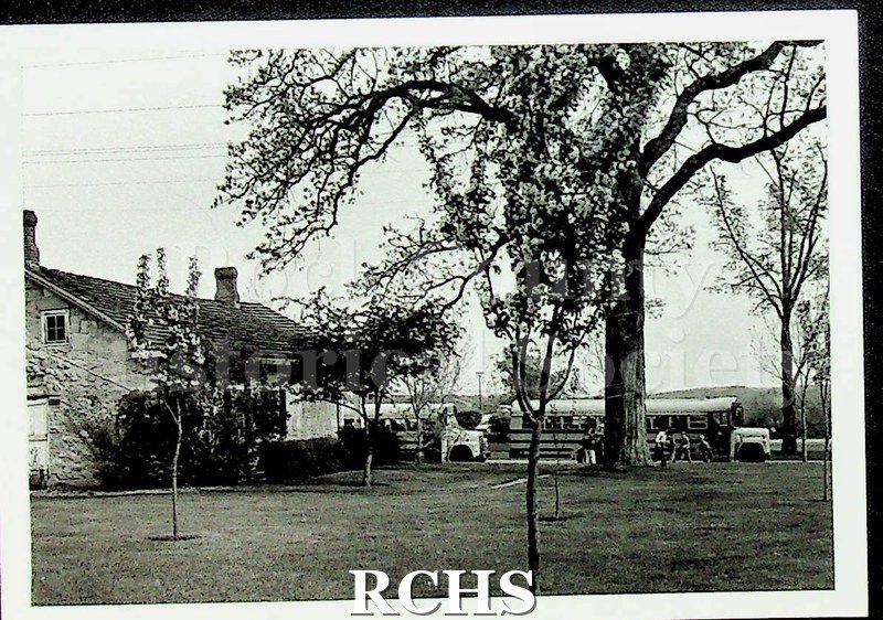 Black and white photograph of unidentified school buses in front of the Stone House taken from the rear of the Stone House.