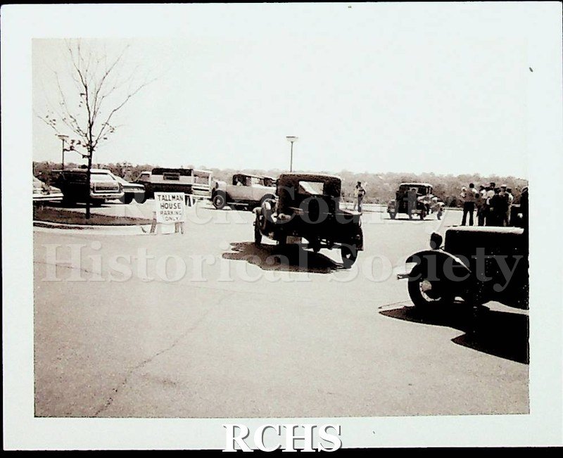 Black and white photograph of Model A Fords driving into the parking area at the Tallman House.