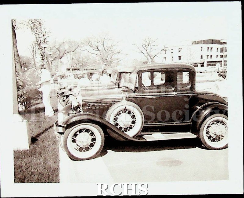 Black and white photograph of Model A Fords parked in front of the Tallman House.