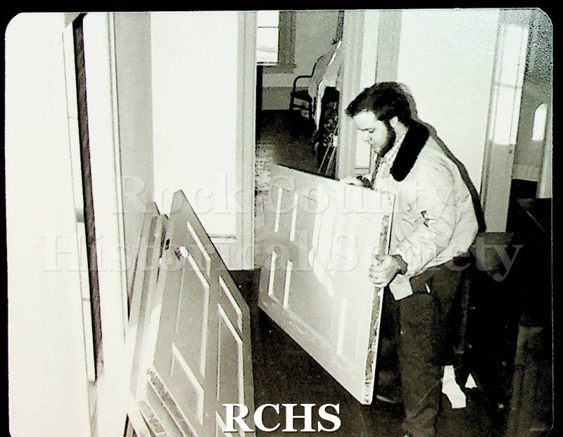 Black and white photograph of Paul Tropp holding a door. There are other doors on the left side of the room.