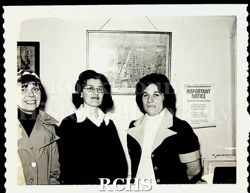 Black and white photograph of Mary Hunt, Judy Hamilton, and Shirley Larson standing in front of a painting with a paper beside it that reads: "Important Notice".