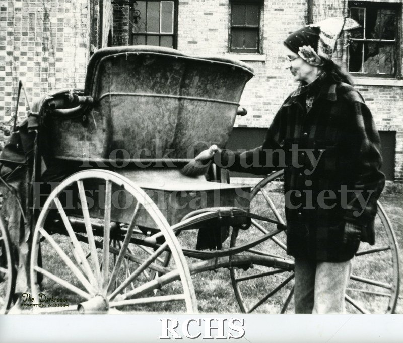 Black and white photograph of Nancy Raufman brushing snow off a sleight with a whiskbroom.