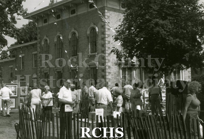 Black and white photograph of the 1983 Tallman Festival. People are standing near the Tallman House. N83013 Strip.