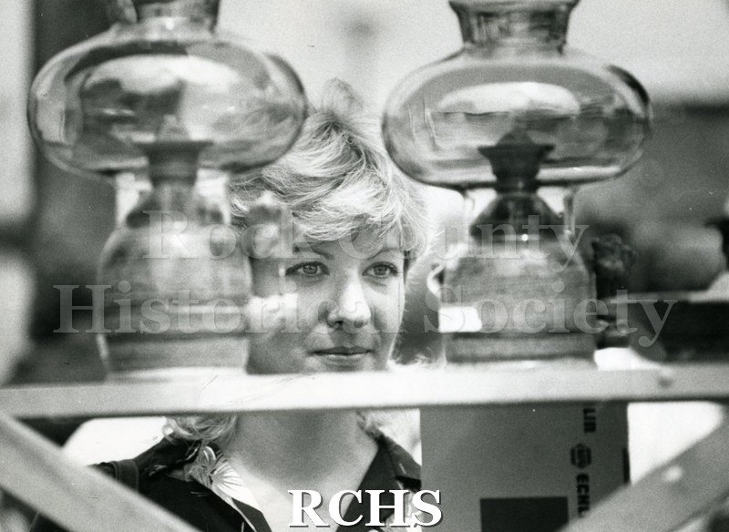 Black and white photograph of Shelly Eagan looking over stoneware oil lamps on exhibit.