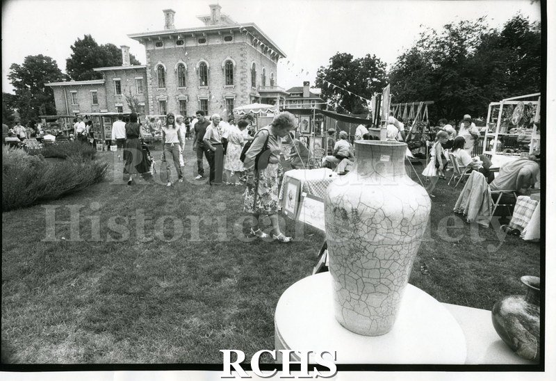 Black and white photograph of the Tallman Festival. Shows people on the grounds of the Tallman House looking at exhibits.