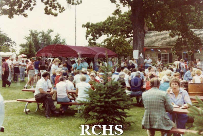 Colored photograph of people sitting at tables and moving around the grounds at the Tallman Art festival.