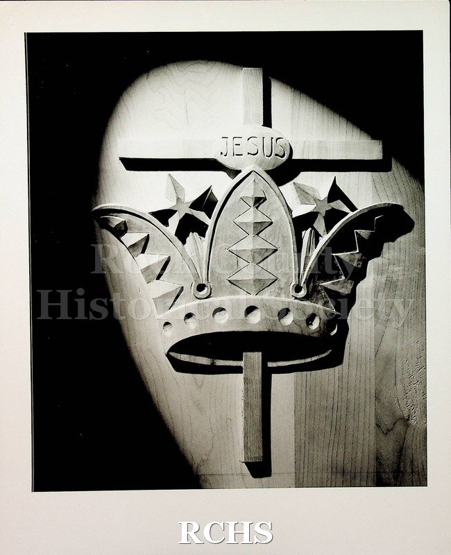 Black and white photograph of crown with a cross inside and the name "Jesus" engraved on it. Made by Ossit Furniture. Photographer: Rex Photo Janesville, Wis.