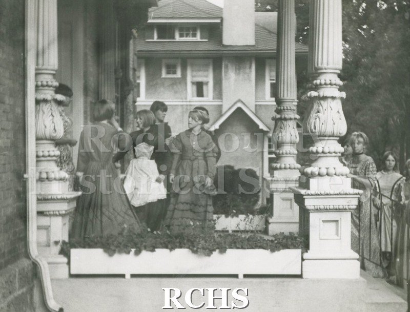 Black and white photograph of Heritage Day, 1966. Shows an unidentified women in costume standing on the porch of the Tallman House.