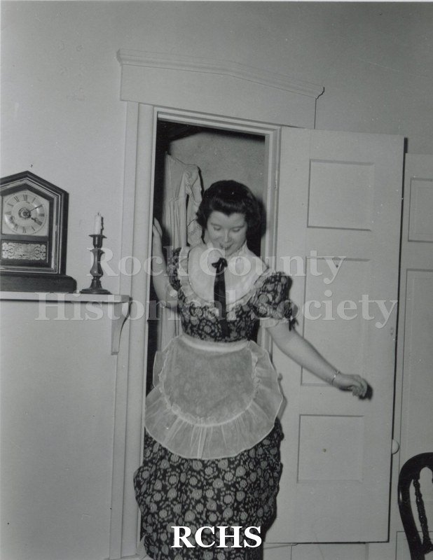 Black and white photograph of a costumed guide coming out of the closet in the Tallman House where there is a secret staircase.