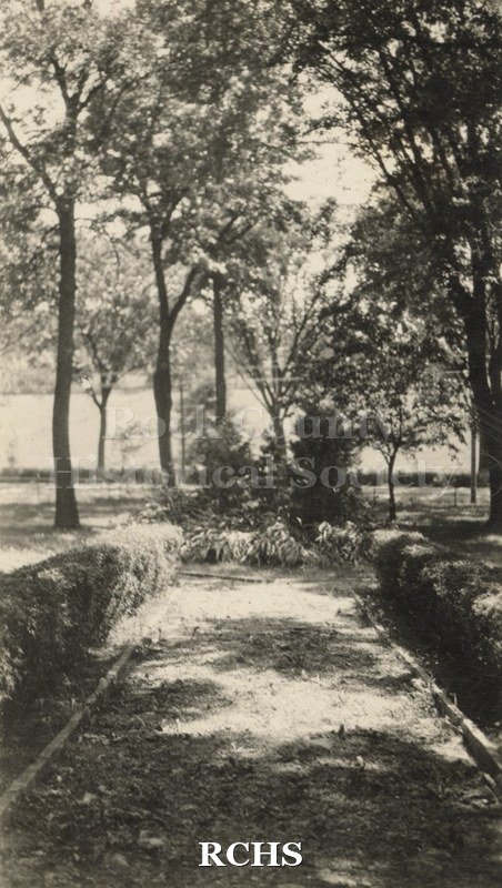 Black and white photograph of Craigknoll. Shows a lane leading to a road. There are trees and shrubbery on either side.