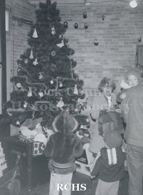Black and white photograph of a decorated Christmas tree with children and adults standing in front of it.