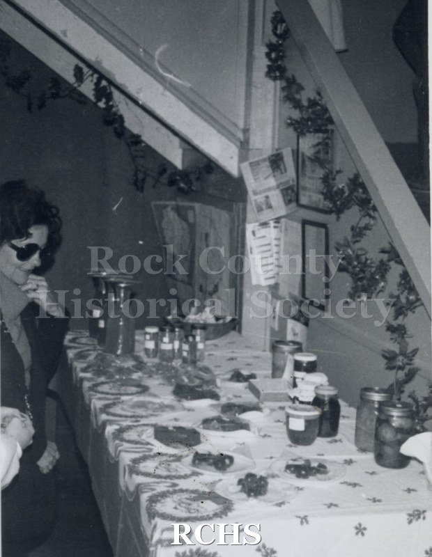 Black and white photograph of a table with Christmas items on it. A woman is contemplating what to buy.