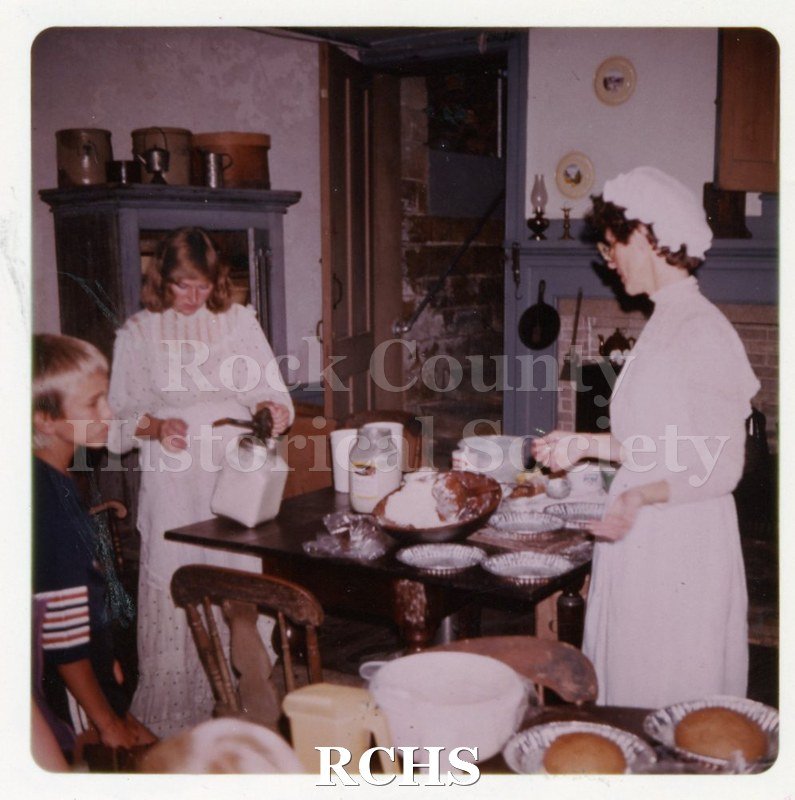 Colored photograph of a breadmaking demonstration at Tallman Festival. Shows two women wearing period costumes. A young boy is looking on.