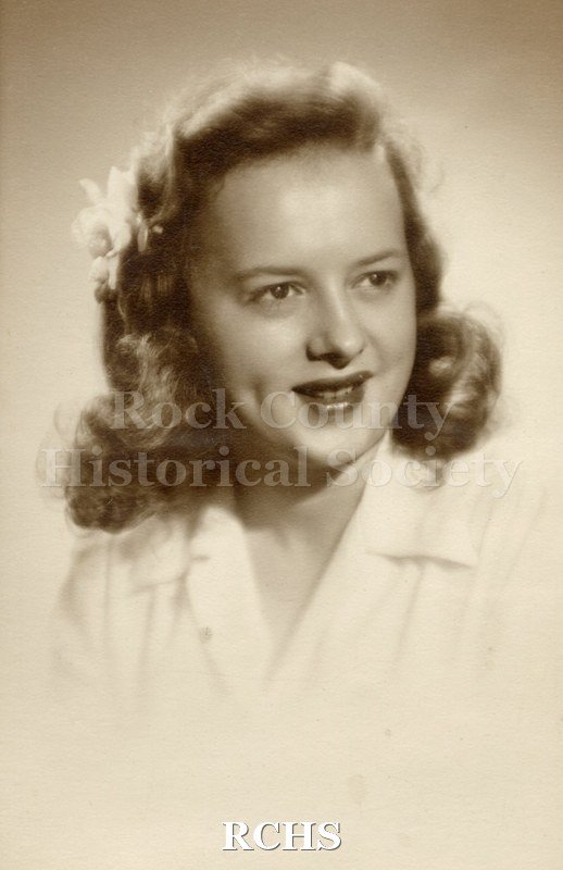 Black and white photograph of Marion McLay Craig wearing a white blouse with a flower in her hair. Her hair is long and curled on the ends.