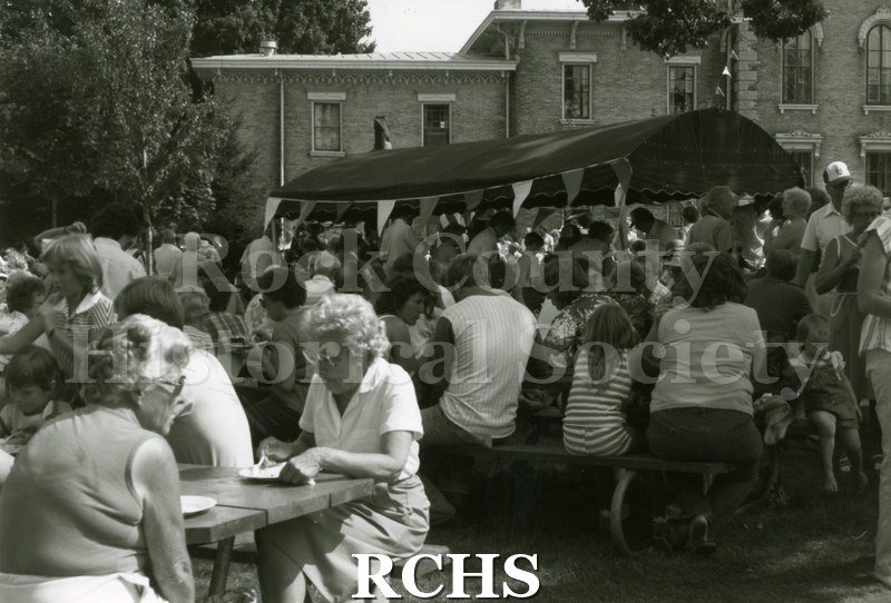 Black and white photograph of the 1983 Tallman Festival. People are sitting at tables eating lunch. N83013 Strip.