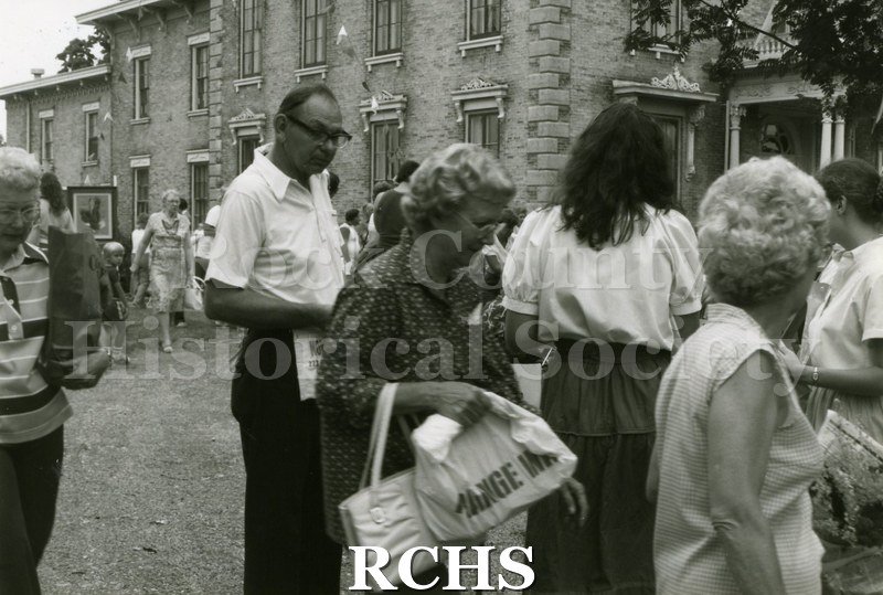 Black and white photograph of the 1983 Tallman Festival. Shows people looking over an exhibit near the Tallman House. N83013 Strip.
