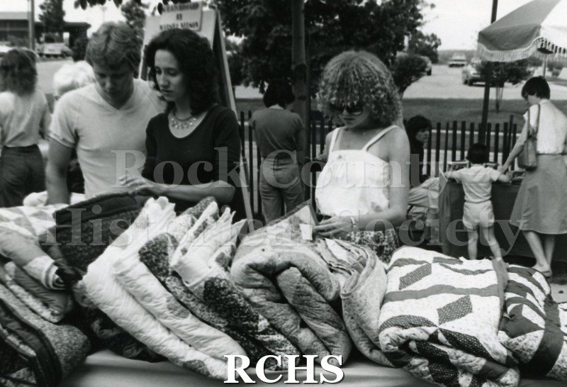 Black and white photograph of people looking at quilts at the Festival.