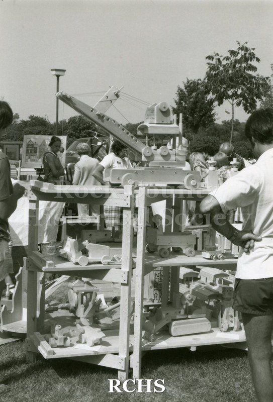 Black and white photograph of an unidentified man looking at an exhibit of wooden toys.