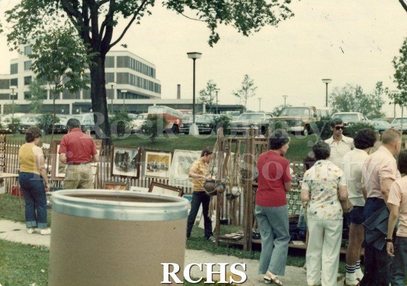 Colored photograph of the 1976 Arts and Crafts Fair. Shows people examining exhibits on the grounds of the Tallman House.