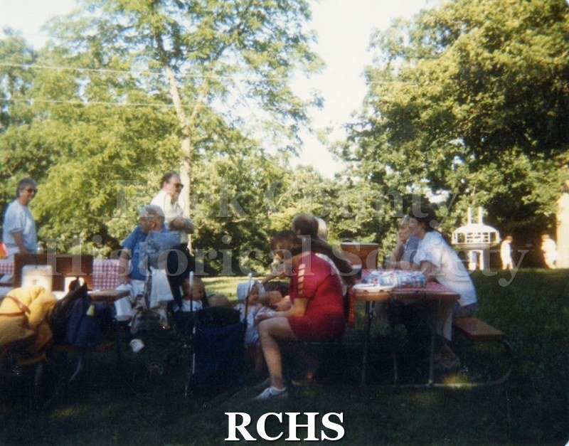 Historic image of Color photogrpah of Rock County Historical Society Picnic. Several unidentified people are seated or standing near the tables.