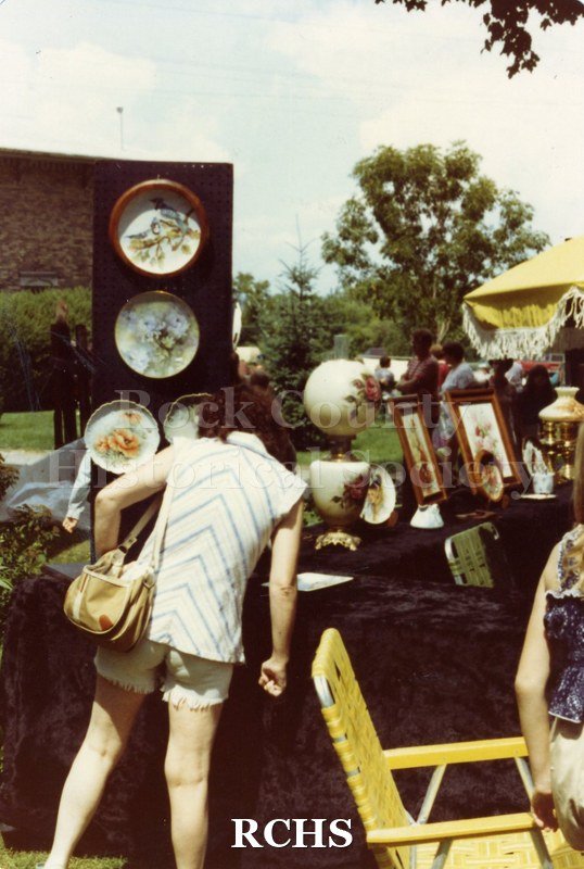 Colored photograph of a woman looking at an exhibit of antiques.
