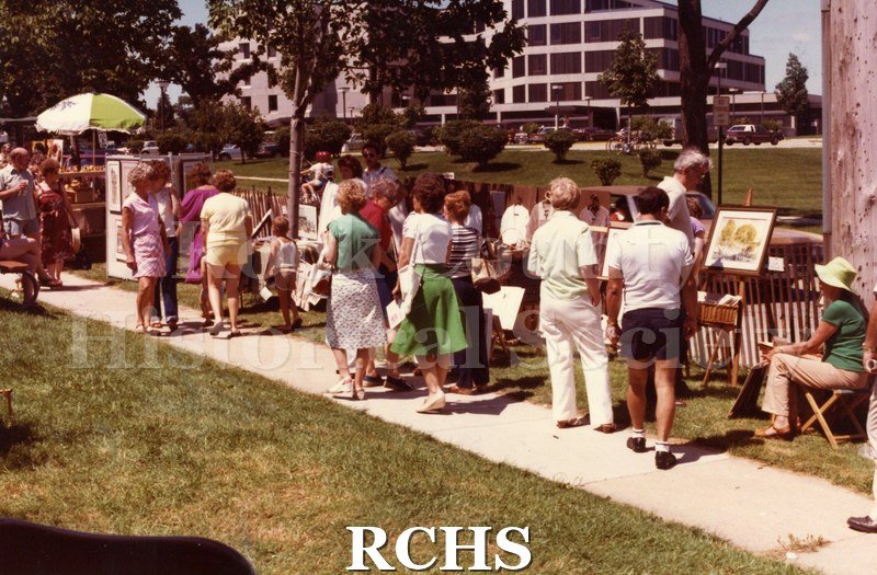 Colored photograph of the 1982 Tallman Arts Festival taken at ground level. There are several people on the sidewalk looking at the exhibits.