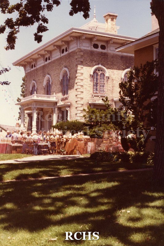 Colored photograph of the Tallman Arts Festival taken at ground level. The Tallman House is visible in the background with the fencing around it.