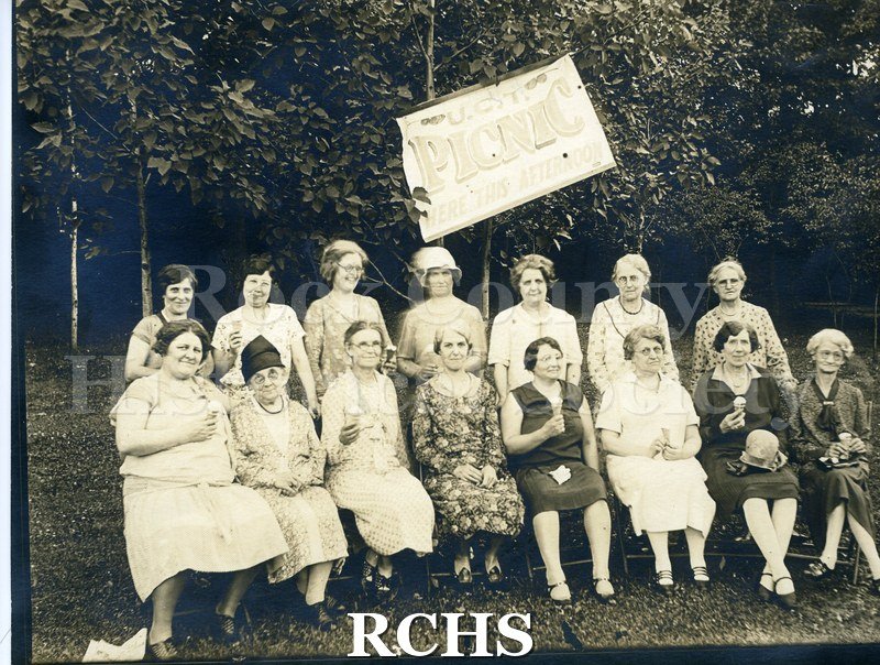 Black and white photograph of the Ladies Auxiliary Janesville Council #108 Picnic. Shows 15 women at a picnic. Seven are standing in the back and eight are seated.