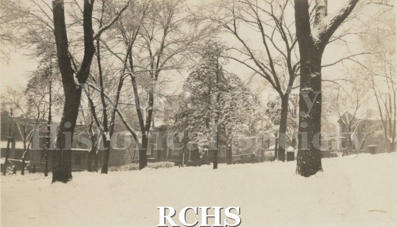Black and white photograph of Woods Flats. Shows a row of houses with snow on the ground and trees in the foreground.