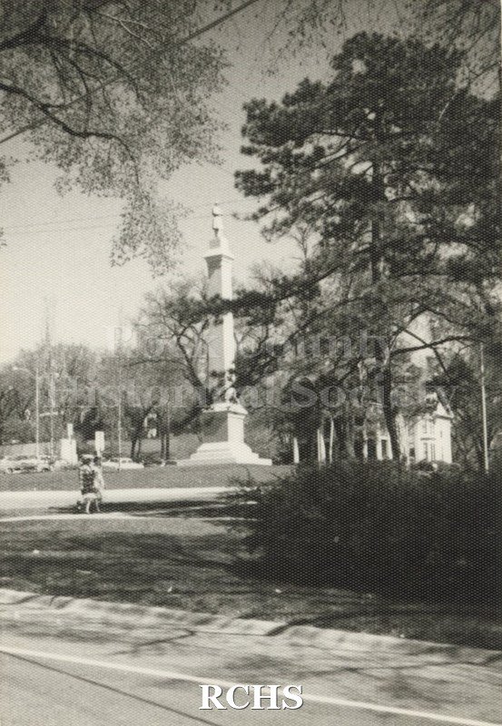 Black and white photograph of Monument in Court House Park. Shows a person walking toward the monument.