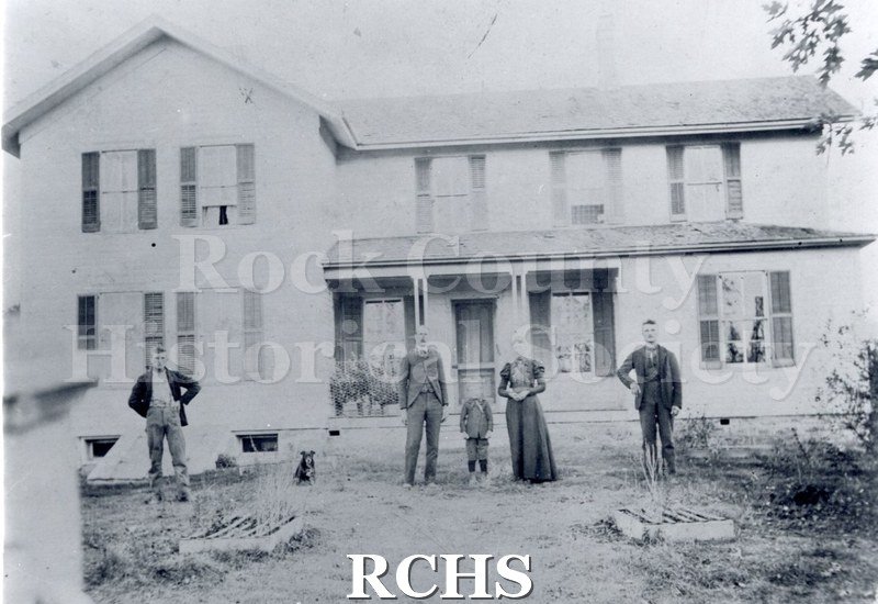 Black and white photograph of the Donald Olson Farm showing a two story farm house with five people standing in front of it.